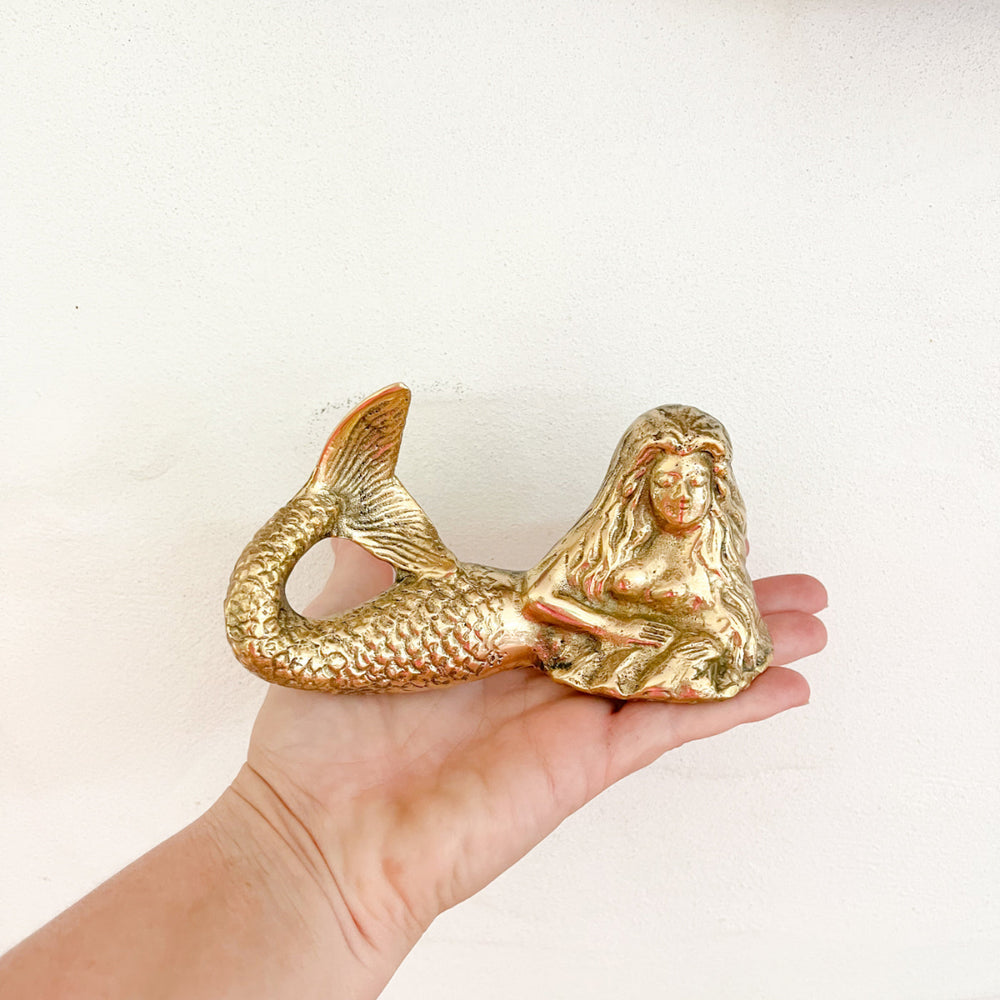 A brass mermaid figurine in a lying position, placed on a hand to show sizing